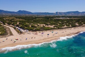 An aerial view of a beach with a row of parked cars, beach umbrellas, and people. - Apartment 'Cerri' with sea view, private terrace, and ferry discount codes (Badesi)