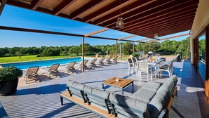 Un patio exterior con piscina, sillones de descanso, zona de comedor y techo de madera.