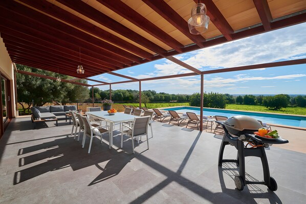An outdoor patio with a pool, a dining area, and a grill.