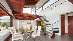 Un interior moderno con una mesa de comedor de vidrio, sillas blancas, una escalera de madera y vistas al exterior.