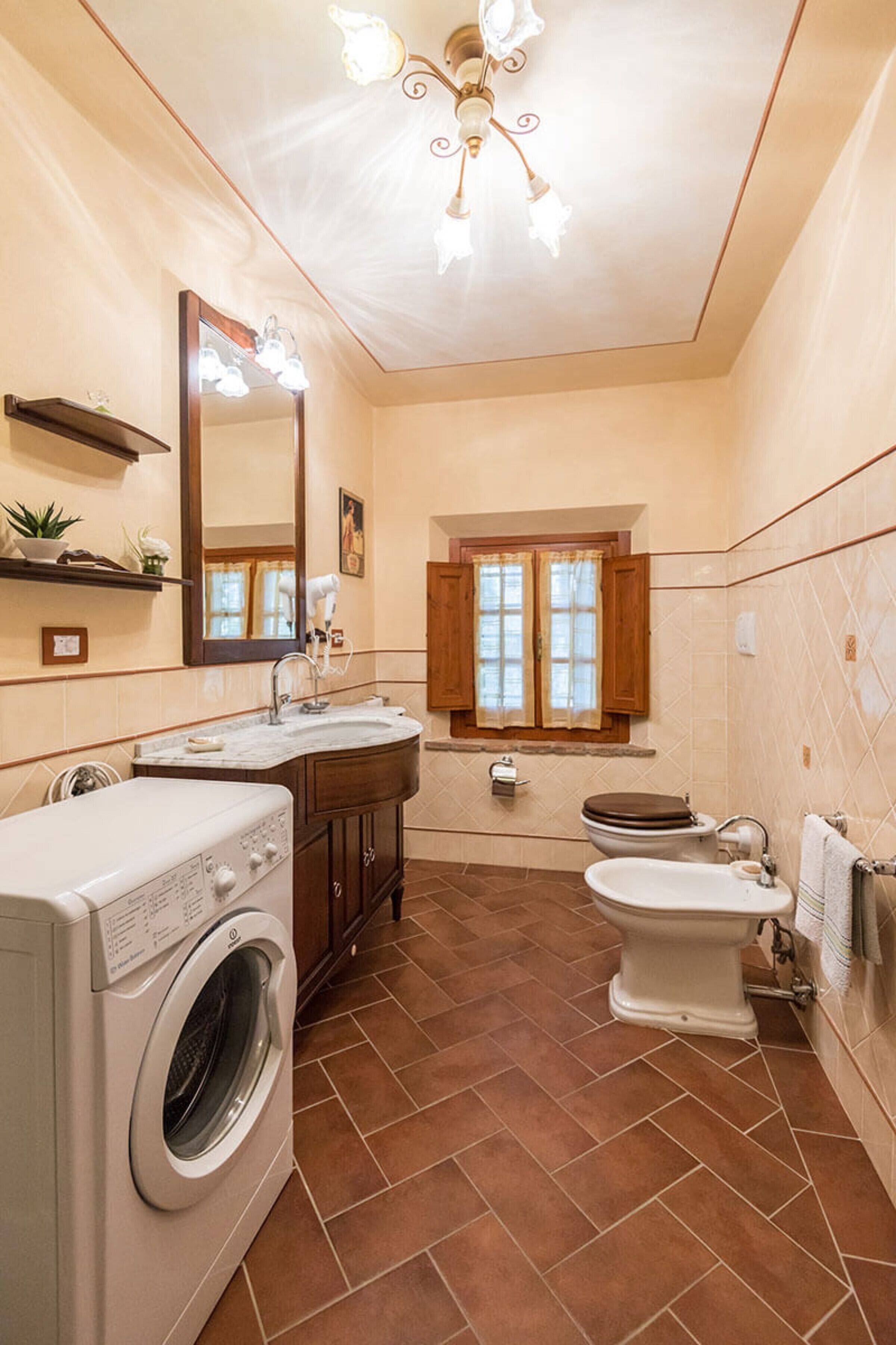 Ein Badezimmer mit Waschmaschine, Spüle, Toilette, Spiegel und einem Fenster mit Vorhängen.