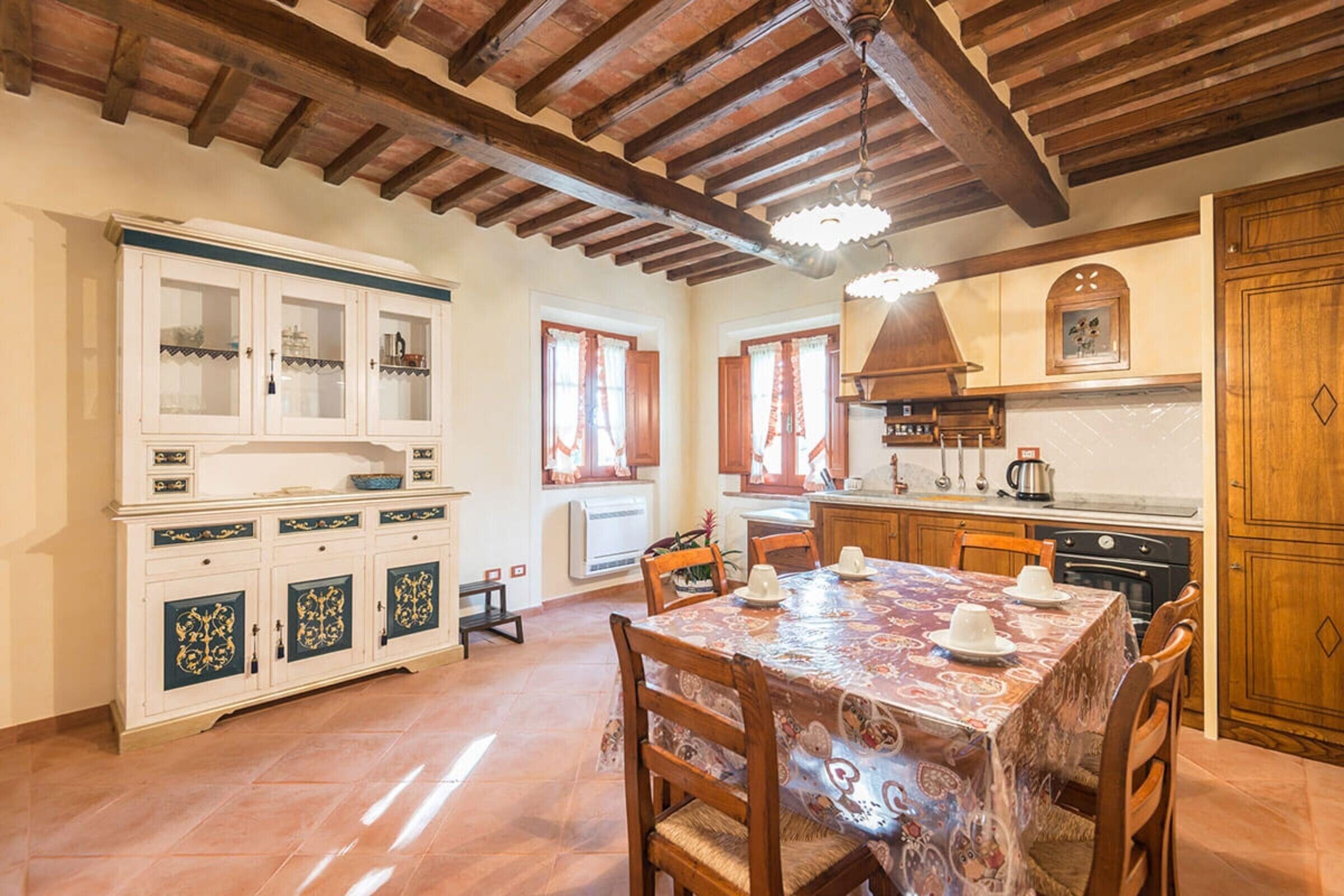 A dining area with a table set for four, wooden chairs, a cabinet with glass doors, and a kitchen area with a stove and cabinets.