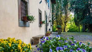 Un edifici amb una banca de pedra, plantes en testos i un camí que condueix a un jardí.