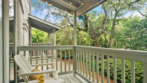 A covered porch with white railings, a bench, and a table with a yellow cup. - Steps Away from the Pool, Beach, Restaurants, Village, and Pier! (Saint Simons Island)