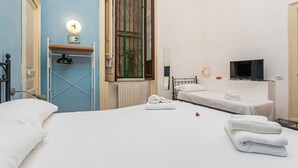 Une chambre d’hôtel équipée d’un lit, d’une télévision, d’une fenêtre avec des rideaux, d’un radiateur et d’un porte-serviettes.