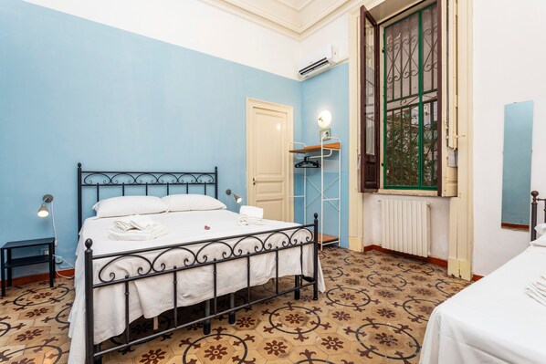 Un dormitorio con cama, mesita de noche, radiador, ventana y puerta.