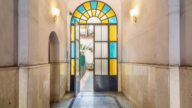 Un couloir doté d’un sol carrelé, d’une porte en verre avec un portail en métal et d’un luminaire fixé au mur.