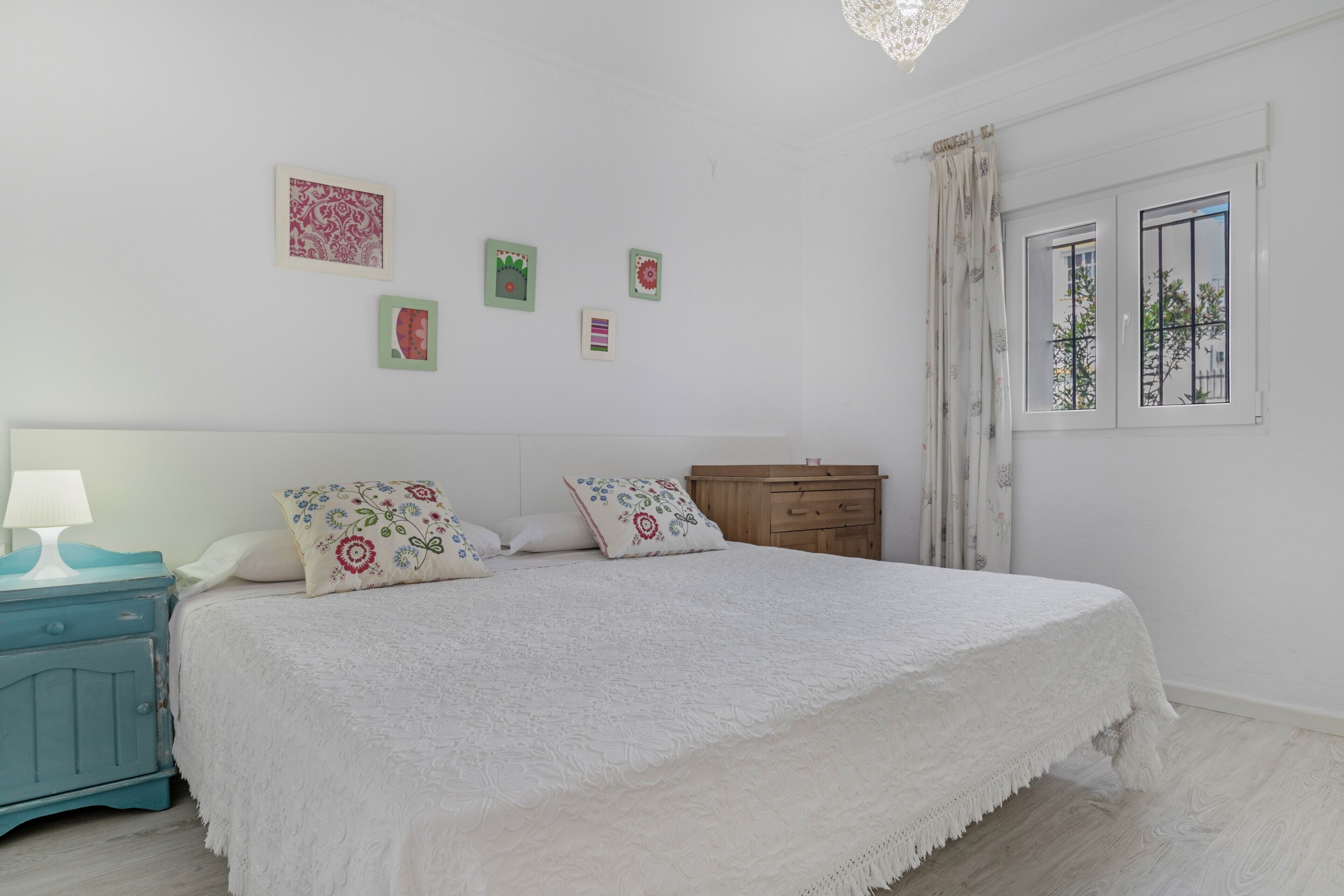 A bedroom with a bed, a nightstand, a dresser, and a window with curtains.
