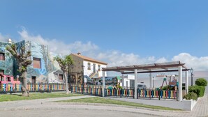 A playground with colorful equipment, a covered seating area, and a mural on a building.