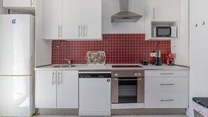 A kitchen with white cabinets, a dishwasher, an oven, a microwave, and a red-tiled backsplash.