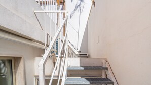 Una escalera estrecha con barandillas blancas y una barana de metal, que conduce a un piso superior.