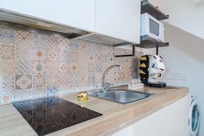 Una cocina con un salpicadero decorativo, un lavamanos de acero inoxidable, un microondas y una lavadora.