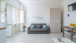 Una sala moderna con un sofá gris, una mesa de centro blanca, una mesa de comedor de madera y un cartel en la pared que dice 'Welcome to our home'.