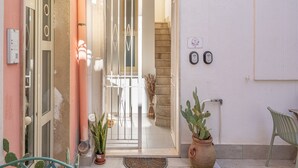 A hotel entrance with a glass door, a potted plant, a chair, and a wall-mounted device. - Apartment 'I Sogni Di Ludo' with Shared Terrace, Wi-Fi and Air Conditioning (Siracusa)