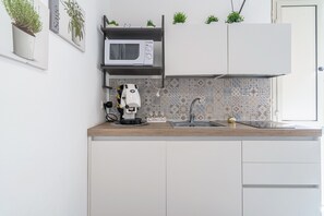 Una cocina moderna con armarios blancos, microondas, cafetera y fregadero.