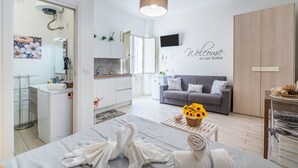 A modern living room with a grey sofa, a coffee table with sunflowers, a TV mounted on the wall, and a 'Welcome to our home' sign. - Apartment 'I Sogni Di Ludo' with Shared Terrace, Wi-Fi and Air Conditioning (Siracusa)