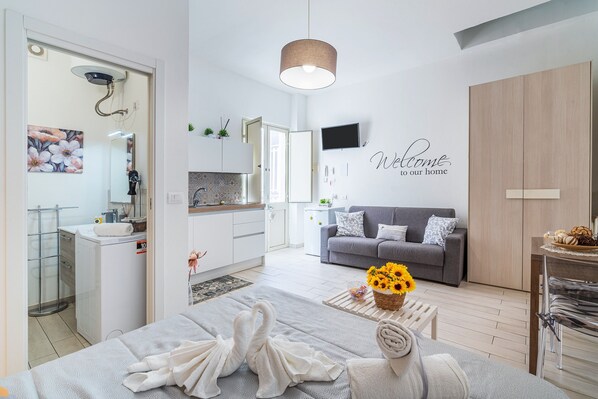 Un salón moderno con un sofá gris, una mesa de centro con girasoles, un televisor montado en la pared y un cartel que dice 'Welcome to our home'.