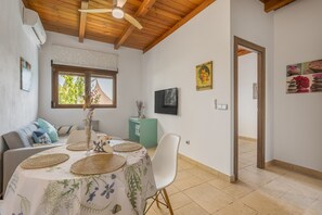 Un coin repas avec une table dressée pour deux personnes, un ventilateur de plafond, une fenêtre avec vue et une porte donnant sur une autre pièce.