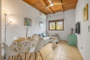 Un salon comprenant un canapé, une table à manger avec des chaises, une petite table basse, un ventilateur de plafond et un téléviseur fixé au mur.