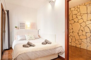 Une chambre à coucher avec un lit, des oreillers, une lampe fixée au mur et un mur en pierre.