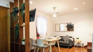 A modern living room with a dining area, a grey sofa, a small side table, and a TV mounted on the wall.
