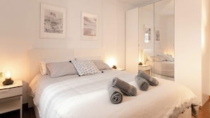 A neatly made bed with rolled towels, a bedside table with a lamp, and two framed pictures on the wall.