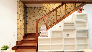 A staircase with a stone wall and wooden railing, leading to a white shelving unit with multiple compartments.