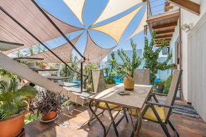 An outdoor patio with a table and chairs, surrounded by potted plants and a large umbrella.