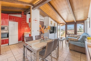 A modern kitchen with red cabinets, a dining table with chairs, and a living area with a sofa and TV.