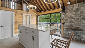A modern kitchen with a central island, wooden ceiling beams, and a stone accent wall.
