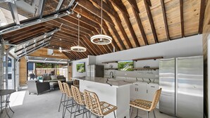 A modern kitchen with a large island, bar stools, stainless steel appliances, and a wooden ceiling.