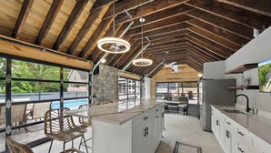 A spacious kitchen with a large island, white cabinetry, and a view of a swimming pool.