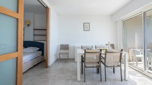 A modern room with a bed, a dining table with chairs, a small kitchen area, and a sliding glass door leading to an outdoor area. - 2-Br Seafront Apartment in Cannes (Cannes)