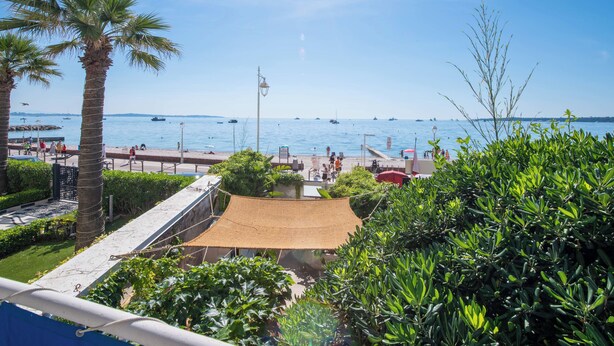 A coastal view with palm trees, a beach, and boats on the water. - 2-Br Seafront Apartment in Cannes (Cannes)
