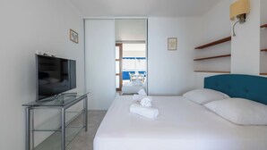 A hotel room with a bed, a TV on a glass table, a bathroom visible through an open door, and a view of the sea. - 2-Br Seafront Apartment in Cannes (Cannes)