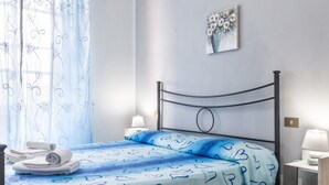 A neatly made bed with a blue heart-patterned bedspread, a metal headboard, and a wall-mounted artwork above it. - Room 'Corbezzolo' with Shared Garden and Wi-Fi (Grosseto)