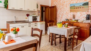 A kitchen with white cabinets, a microwave, and a dining area with a table and chairs. - Room 'Corbezzolo' with Shared Garden and Wi-Fi (Grosseto)