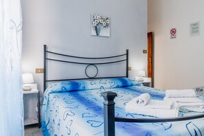 A neatly made bed with a blue heart-patterned bedspread, a bedside lamp, and a wall-mounted artwork of flowers.