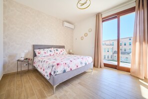 Un dormitorio con cama, mesita de noche, ventana con cortinas y vistas a edificios.