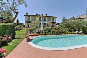 A swimming pool with a brick deck, surrounded by a well-maintained garden and a large building with a tiled roof. - Villa 'Antica Sosta Renai' with Private Pool, Terrace and Wi-Fi (Castelfiorentino)
