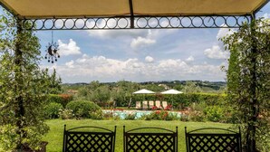 Un patio cubierto con vistas a una piscina, jardín y paisaje distante.