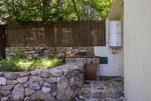 A stone planter with plants, a stone wall, a wooden fence, and a water heater mounted on a wall.