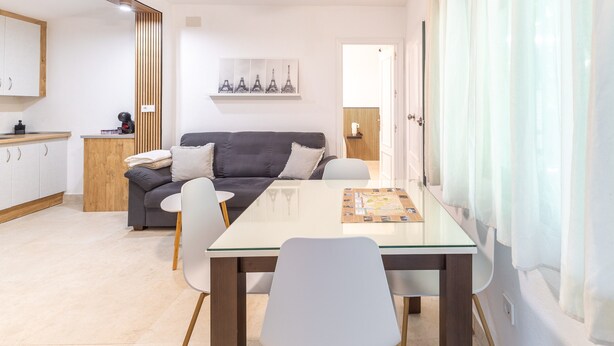 Una sala de estar moderna con una mesa de comedor de vidrio, un sofá y una zona de cocina al fondo.