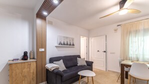 Una sala moderna con un sofá oscuro, una pequeña mesa redonda y un aparador de madera.