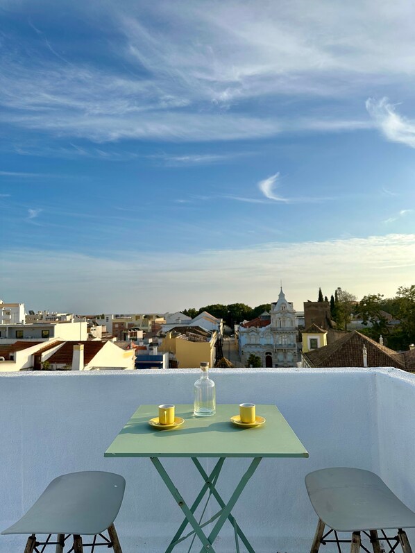 Una mesa con dos sillas y una botella en un balcón con vista a un paisaje urbano que incluye edificios y una iglesia.