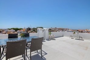 Una terraza en la azotea con una mesa de vidrio, sillas de mimbre, una pequeña planta en maceta y vistas de la ciudad.