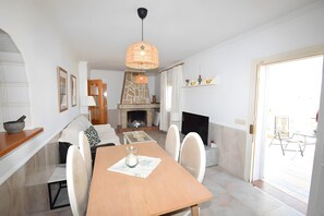 Un espace repas comprenant une table en bois, des chaises, un luminaire suspendu, une cheminée et un téléviseur.