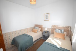 Une chambre avec deux lits, une table de chevet, une lampe, un tableau encadré au mur et une porte en bois.