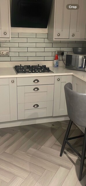 Une cuisine avec des armoires blanches, une cuisinière à gaz, un four à micro-ondes et une chaise.