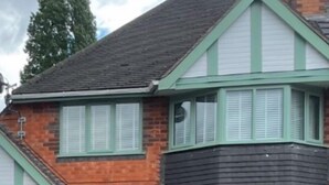 Een herenhuis met twee verdiepingen, gebouwd uit baksteen, met een groene deur, meerdere ramen voorzien van luiken en een kleine voortuin.